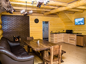 Гостиная в коттедже Банная Усадьба. Телевизор, кухонная зона, диван, стол